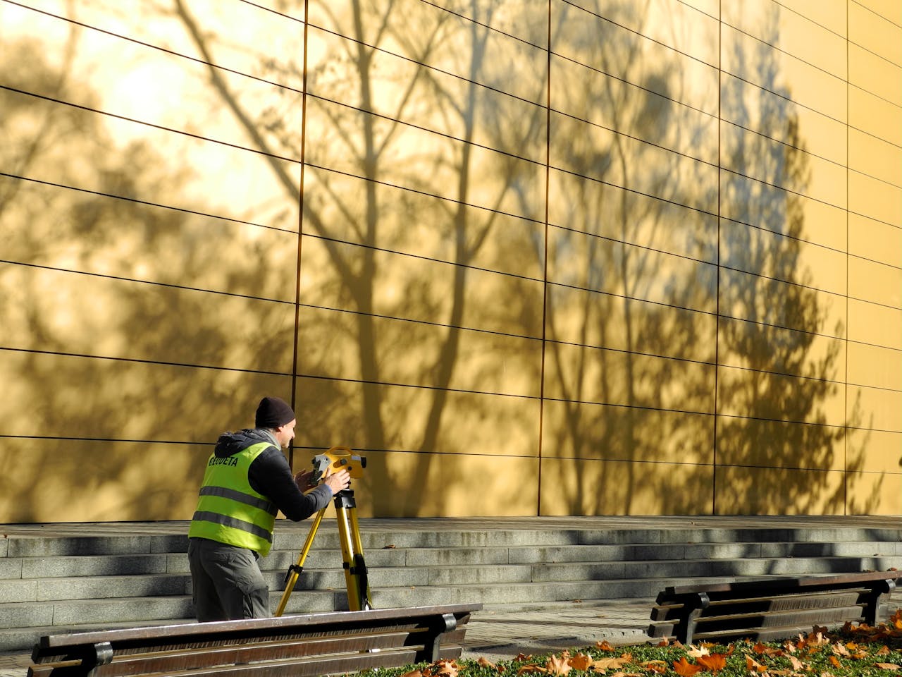 services-03 Surveyor working with equipment outdoors by a gold reflective wall during daytime.