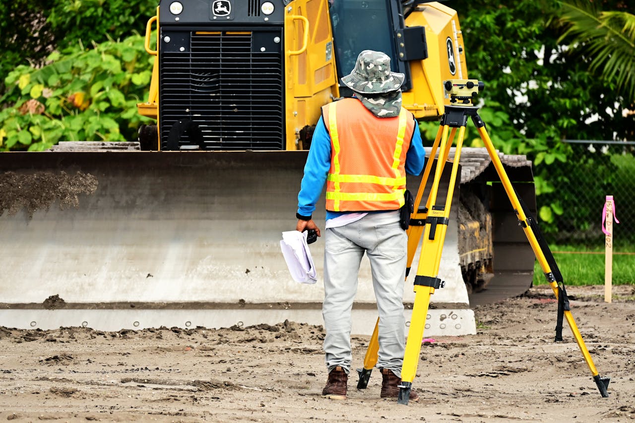 services-02 Surveyor with equipment at an active construction site, observing bulldozer operations.