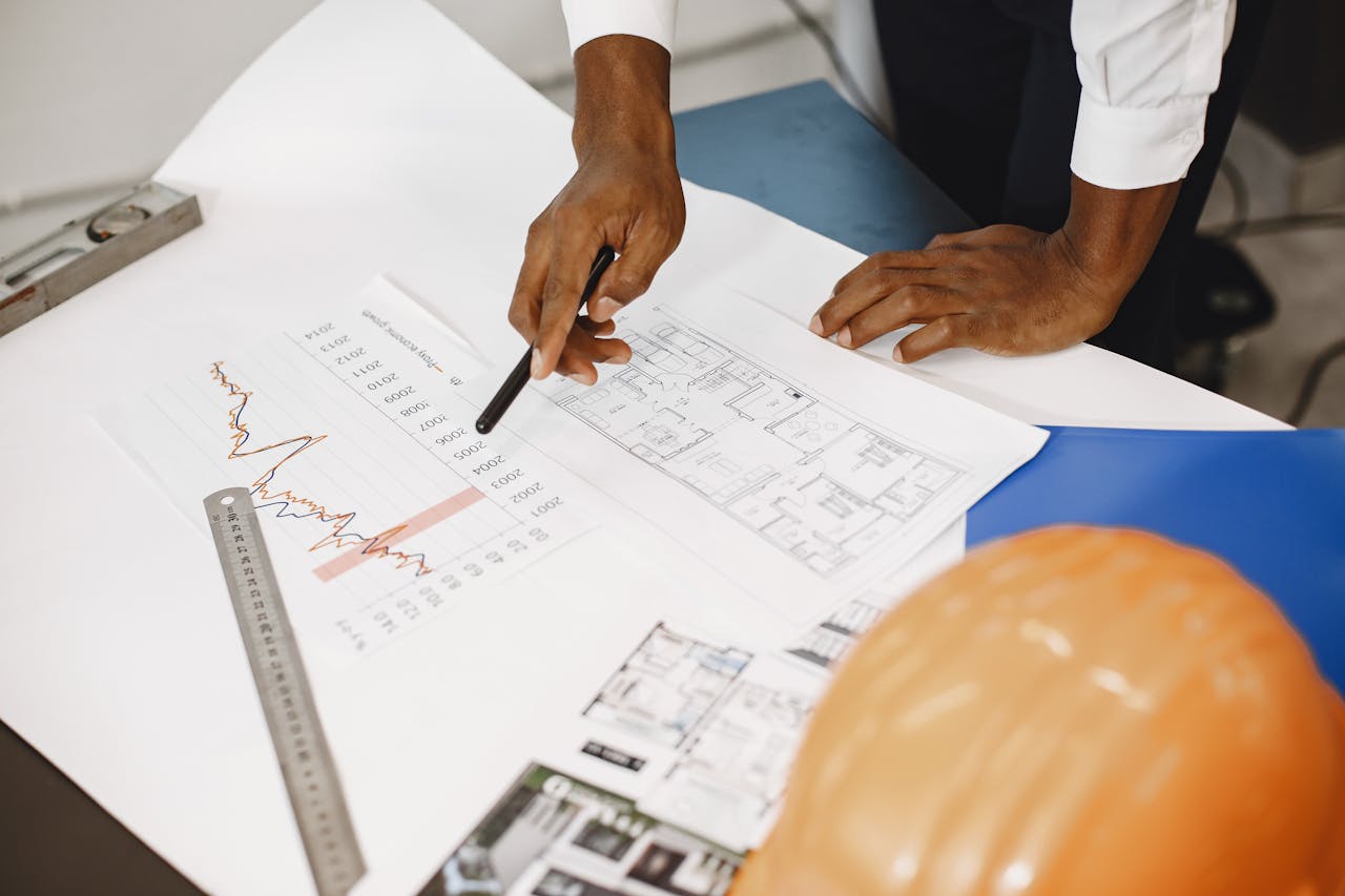 services-03 Hands of an architect analyzing blueprints and financial graphs at a desk.